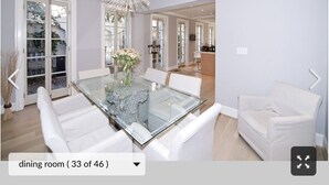 Ein Esszimmer mit einem Glastisch, weißen Stühlen und einer Pendelleuchte.