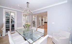 A dining room with a glass table, white chairs, and a chandelier.