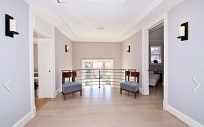 A spacious hallway on the second floor with a view to a balcony, two chairs, and a door leading to another room.