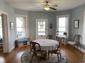 A dining area with a round table, four chairs, a ceiling fan, and a view of the outdoors through large windows.
