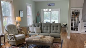 Uma sala de estar com ventilador de teto, um sofá, uma poltrona, uma mesa de centro e um tapete estampado.