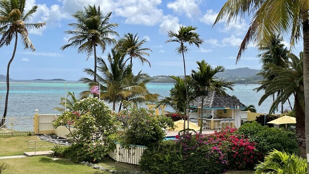 Een tropisch resort met een zwembad, palmbomen en uitzicht op de oceaan.