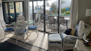 Een ruim balkon met een glazen deur naar een zwembadgedeelte, voorzien van witte rieten stoelen en een glazen tafel.