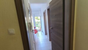 A hallway with a tiled floor, a door on the right, and a view of a balcony with outdoor furniture.