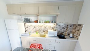 A compact kitchen with white cabinets, a microwave, a sink, and a red chair.