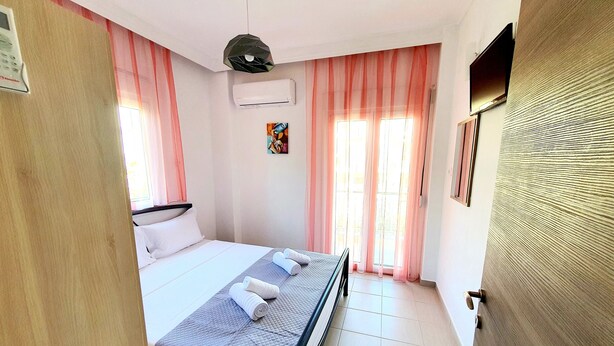 A hotel room with a bed, a bedside table, an air conditioning unit, a window with curtains, and a door.