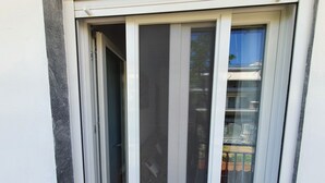 A sliding glass door with a metal screen, leading to a balcony with a view of a building and some greenery.
