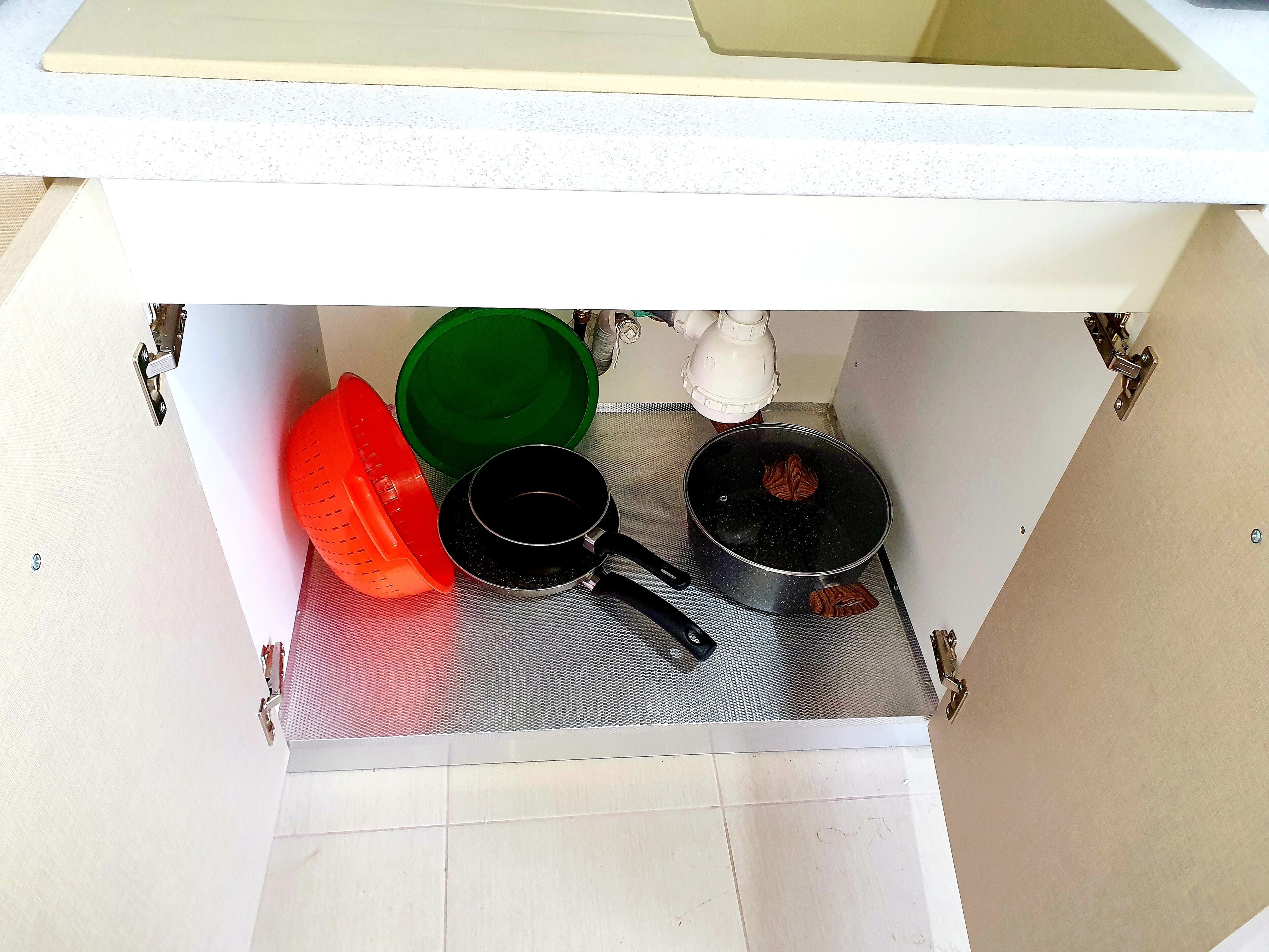 A kitchen counter with a white sink, a metal strainer, a black pot, a green bowl, and a red colander.