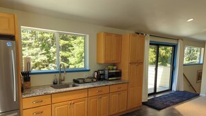 A modern kitchen with wooden cabinets, a stainless steel refrigerator, and a large window providing a view of trees. - Asian-themed Queen's Loft Apartment 10 mins to the beach and downtown! (GUALALA)