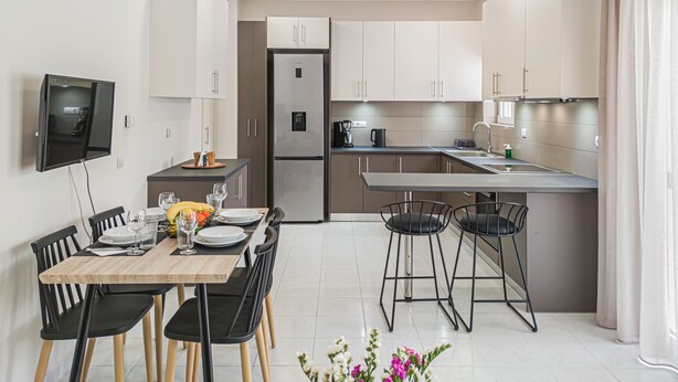 A modern kitchen with a dining area, featuring a built-in oven, refrigerator, and a flat-screen TV mounted on the wall. - Fully renovated apartment in the city centre of Chania with a roof garden! (Χανιά)