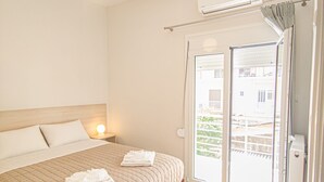 A hotel room with a bed, a nightstand, a wall-mounted air conditioner, and a sliding glass door leading to an outdoor area. - Fully renovated apartment in the city centre of Chania with a roof garden! (Χανιά)