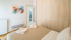 A bedroom with a bed, a bench, a radiator, a wooden wardrobe, and a painting on the wall. - Fully renovated apartment in the city centre of Chania with a roof garden! (Χανιά)
