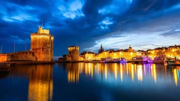 A historic waterfront cityscape with illuminated buildings and a prominent tower reflecting on calm water.