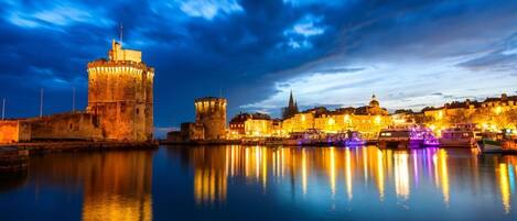 A historic waterfront cityscape with illuminated buildings and a prominent tower reflecting on calm water.