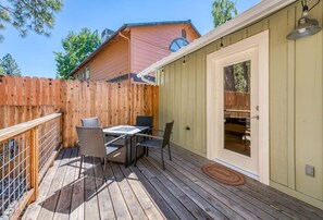 Eine Holzterrasse mit Tisch und Stühlen, ein Holzzaun und ein Gebäude mit Tür und Fenstern.