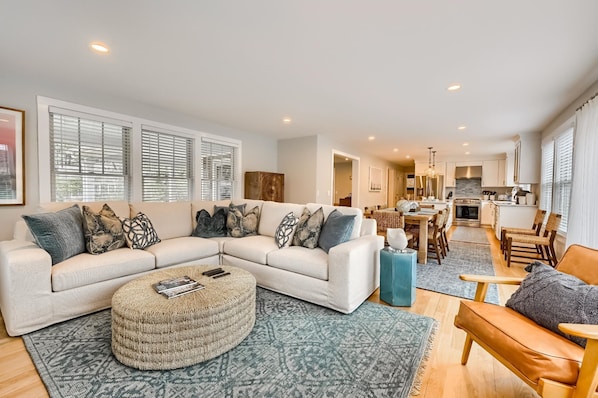 A modern living room with a sectional sofa, ottoman, and a dining area with chairs and a table.