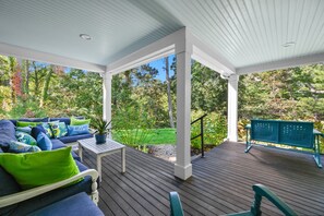 A covered outdoor deck with a wooden floor, a blue sofa with green cushions, and a green bench.
