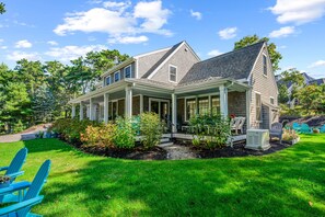 Ein zweigeschossiges Haus mit überdachter Veranda, einem Vorgarten mit saftigem Rasen und einer kleinen Gartenanlage.