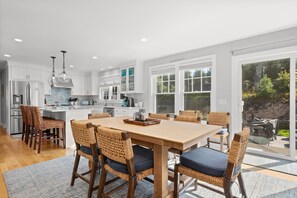A modern kitchen with white cabinetry, a central island, and a dining area with wicker chairs.