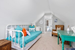 A cozy bedroom with a bed, a chair, a table, and a door leading to another room. - Chatham Luxury Retreat—Porch, Art & Family Fun (Chatham)