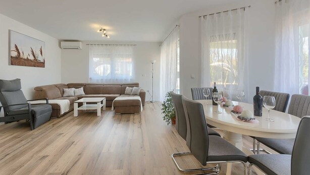 Ett modernt vardagsrum med en soffa, ett soffbord och en matplats med stolar och ett bord.