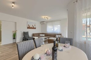 A modern living room with a round dining table, grey upholstered chairs, a brown sofa with patterned cushions, and a painting on the wall. - 3 BD Villa with Private pool, surrounded by greenery (Buje)