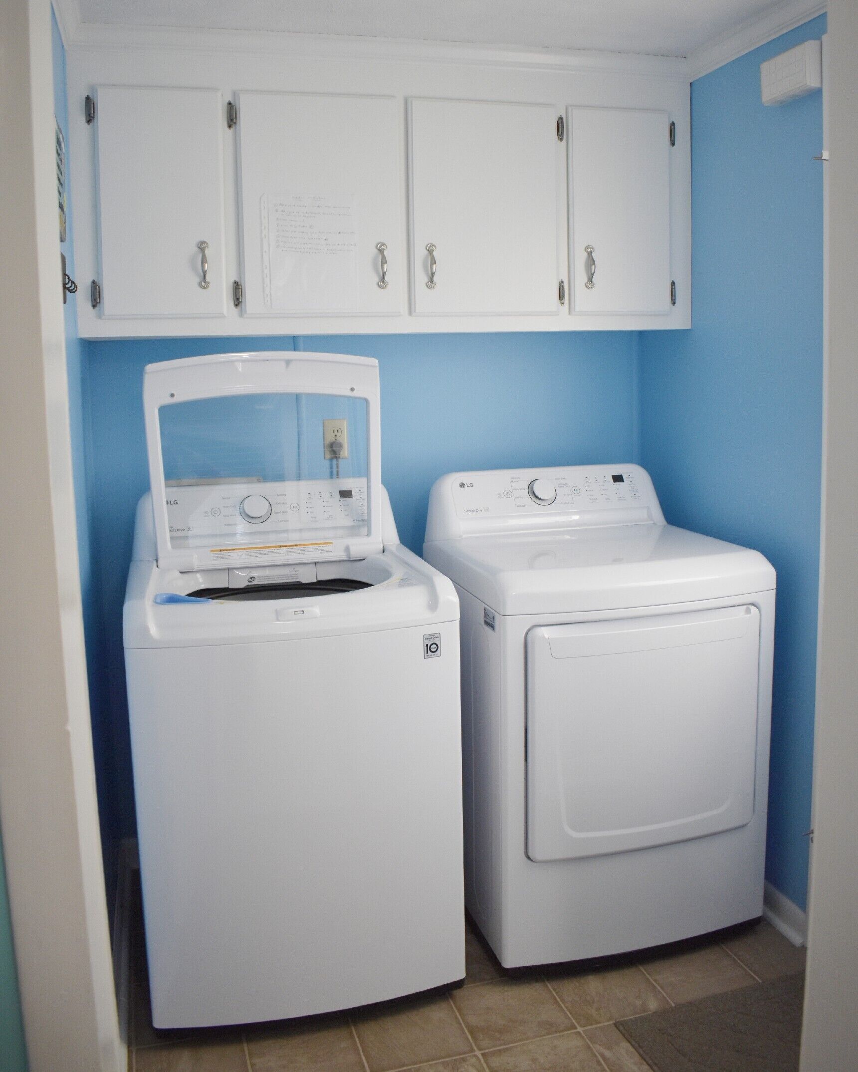 Une buanderie équipée de deux machines à laver et de deux sèche-linge à chargement frontal, tous deux de couleur blanche, avec un mur bleu et des placards blancs au-dessus.