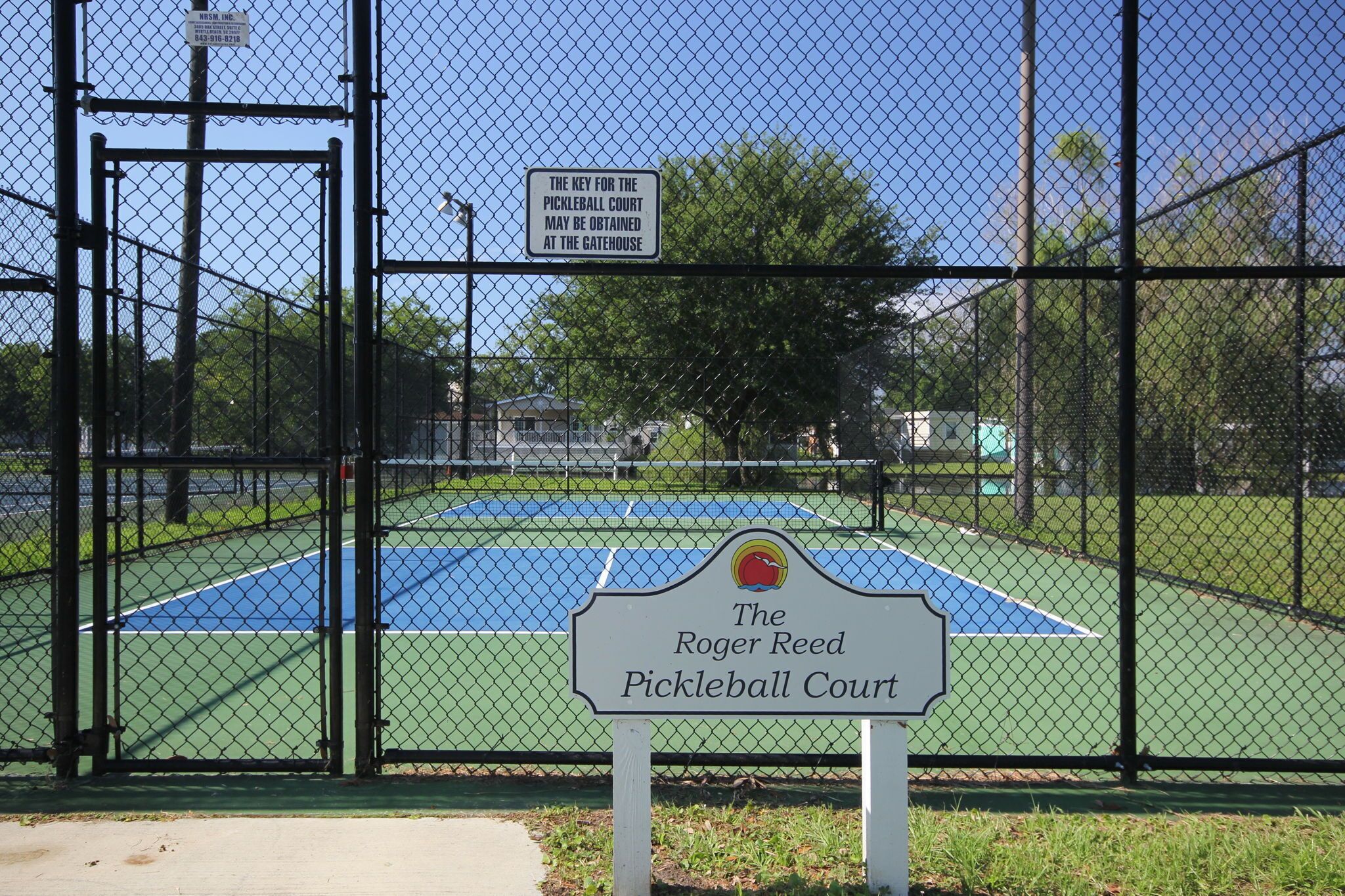 Pista de tenis tancada per una tanca, amb un senyal que indica que és la pista de paleta base Roger Reed.
