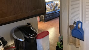 Een keuken met een koffiezetapparaat, prullenbak en een kom met eten op het aanrecht.