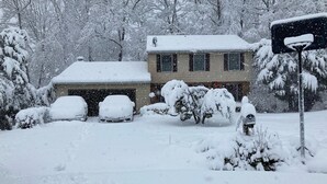 Een huis met een garage, omringd door met sneeuw bedekte bomen en struiken.