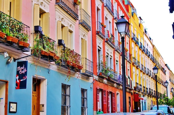 Uma fileira de edifícios coloridos com sacadas, um lampião e uma placa com a inscrição 'Mad Café'.
