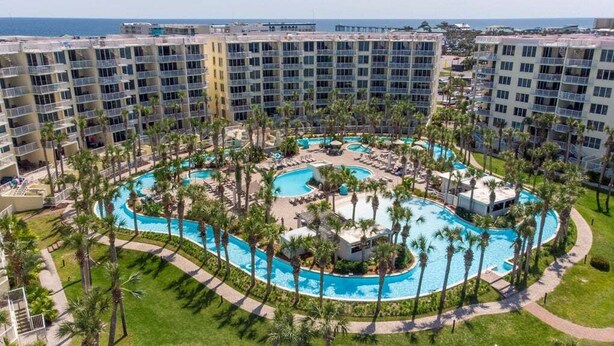 Un hotel de varios pisos, con una piscina central y palmeras aledañas.