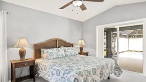 Quarto com cama, duas mesas de cabeceira, ventilador de teto e vista para uma piscina ao ar livre.