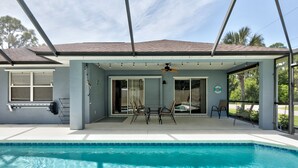 Área da piscina coberta com ventilador de teto, mesa com cadeiras e vista para a paisagem ao redor.