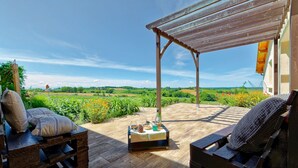 A covered patio with a wooden table set for two, overlooking a scenic countryside view. - Charming 9-person gîte with heated swimming pool (Peyrusse-Grande)