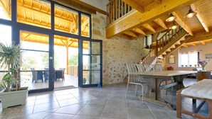 A spacious indoor area with a large open door leading to a balcony, a dining table with chairs, and a staircase with wooden beams. - Charming 9-person gîte with heated swimming pool (Peyrusse-Grande)