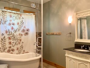 Un baño con bañera, una cortina de ducha con motivos florales, un estante de madera, un perchero en la pared y un tocador con espejo.