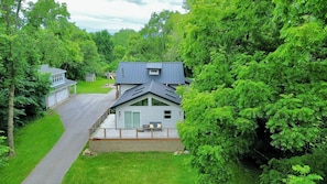 A two-story house with a balcony, surrounded by lush greenery and a driveway.