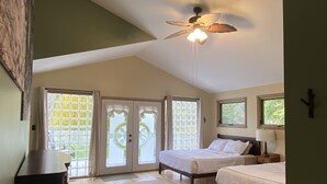 A bedroom with two beds, a ceiling fan, and a large window with a view of greenery.