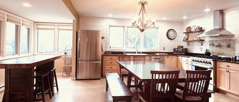 A spacious kitchen with a central island, wooden chairs, a stainless steel refrigerator, and a chandelier.