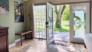 A room with a bench, a door leading outside, a bed, and a wall with a picture.