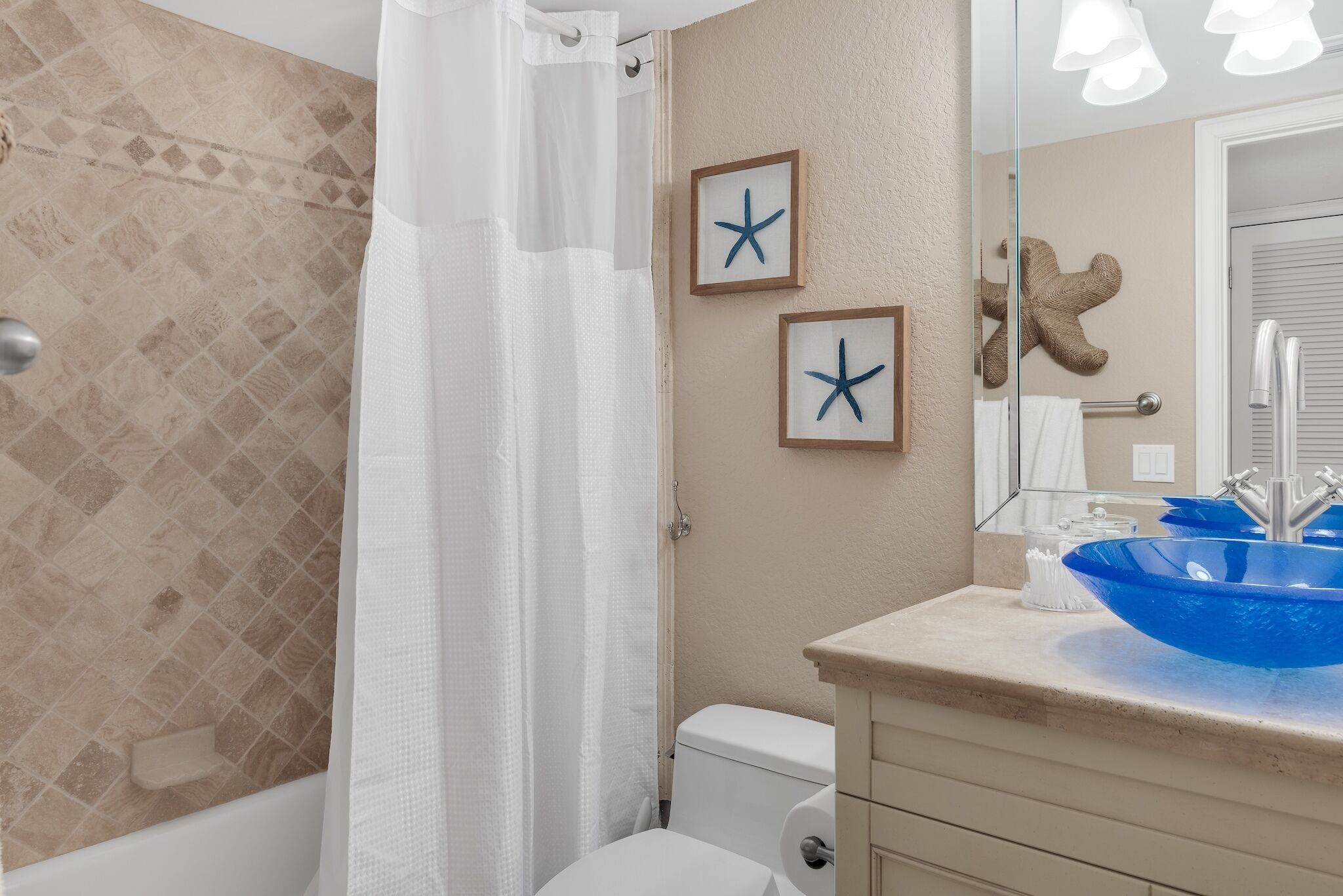 A bathroom with a bathtub, toilet, and sink. There are starfish decorations on the wall and a shower curtain.