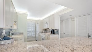 Une cuisine moderne avec des armoires blanches, des comptoirs en granit et un four à micro-ondes encastré.
