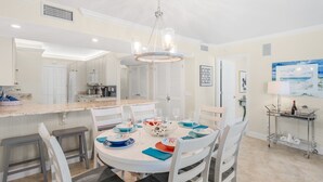 Une cuisine moderne avec des meubles blancs, un îlot central et un coin repas comprenant des chaises blanches et une table ronde prévue pour accueillir six personnes.