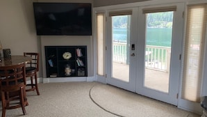 A living room with a flat-screen TV, a fireplace, a bookshelf, and a view of a lake through sliding glass doors. - Waterfront Home-Great Boating/Fishing/Beach. Mountain Views, close to Sandpoint (Sagle)