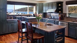 A modern kitchen with dark green cabinets, a central island with bar stools, a view of the lake, and a stove. - Waterfront Home-Great Boating/Fishing/Beach. Mountain Views, close to Sandpoint (Sagle)