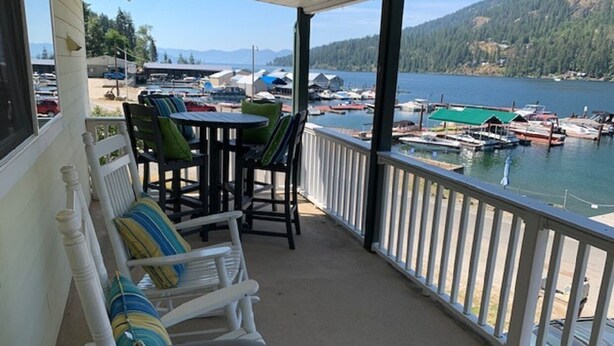 A covered porch with white railings, a table, and chairs with striped cushions. - Waterfront Home-Great Boating/Fishing/Beach. Mountain Views, close to Sandpoint (Sagle)