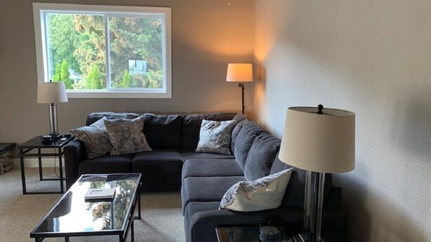 A living room with a sofa, two side tables, a coffee table, and a window with a view of trees. - Waterfront Home-Great Boating/Fishing/Beach. Mountain Views, close to Sandpoint (Sagle)