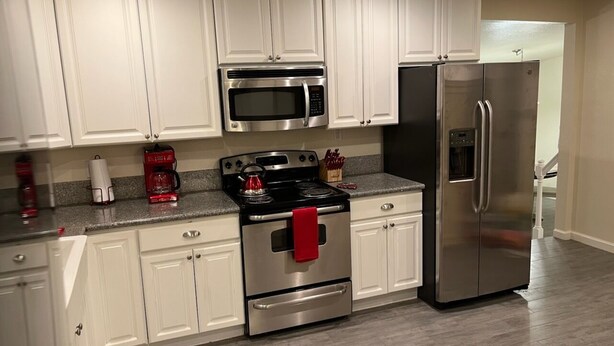 A modern kitchen with white cabinets, stainless steel appliances, and a granite countertop. - 2 bedroom, 2 bath farmhouse (Blythe)