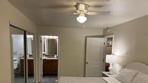 A bedroom with a bed, a ceiling fan, a nightstand, a bedside table, and a bathroom visible through an open door. - 2 bedroom, 2 bath farmhouse (Blythe)